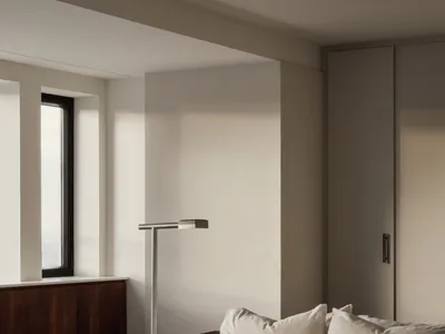 A minimalist bedroom with neutral-colored walls, bedding, and pillows, featuring a simple floor lamp and a window with a view