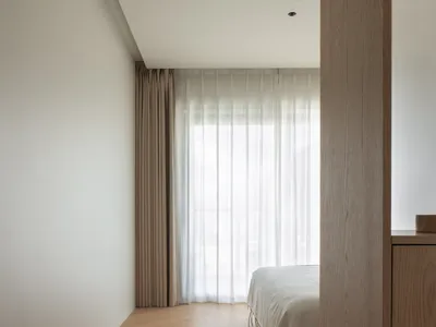 A modern minimalist bedroom with wooden flooring and light-colored curtains.
