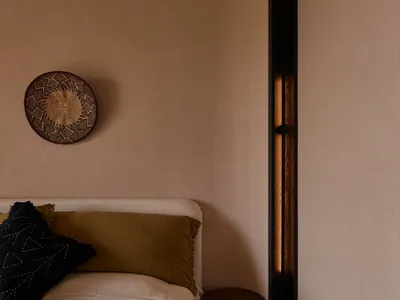Minimalist bedroom with a bed, bedside stool, and decorative basket on the wall.