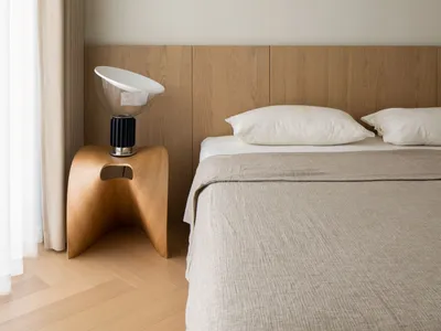 A minimalist bedroom featuring a wooden bedside lamp, a fabric bedspread, and a minimalistic headboard made of wood.