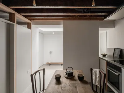 A minimalist residential kitchen with wooden table, concrete walls, and metal accents.