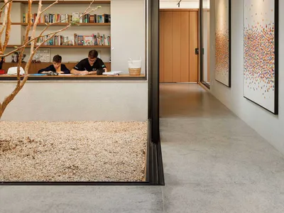 A modern home office space with concrete and glass elements, featuring two individuals working at a desk.