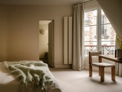 A minimalist bedroom with a bed covered in a green blanket and a white table with a vase of flowers.