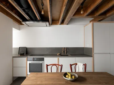 A minimalist residential kitchen featuring a concrete countertop and floor, exposed wooden beams, and modern appliances.