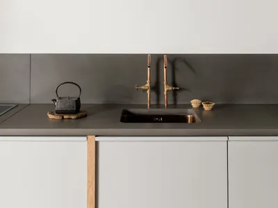 Modern, minimalist kitchen featuring a concrete countertop and exposed wooden ceiling beams.
