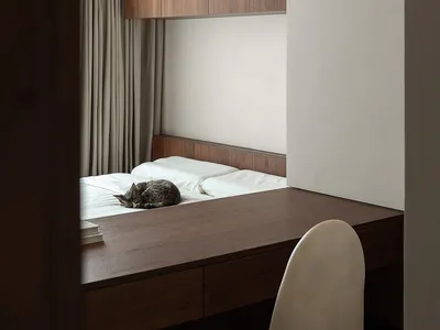 A minimalist bedroom with wooden furniture, including a bed with white bedding, a wooden desk, and a white chair.