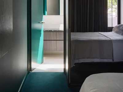 A modern bedroom featuring a glass door leading to an adjacent bathroom with white tiles and wooden cabinetry.