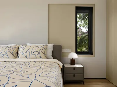 Modern minimalist bedroom featuring a bed with blue and white bedding and a side table with a lamp, set against a neutral col