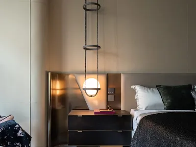 Modern minimalist bedroom with textured leather walls, hanging light fixture, black bedside table, and white bedding.