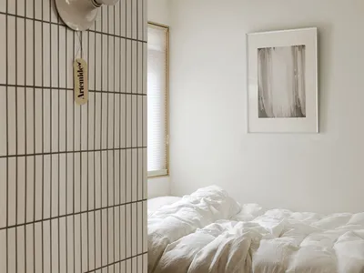 A minimalist bedroom with white tiled walls and a bed covered in white bedding.