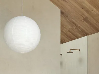 A minimalist bedroom with a white pendant light hanging above the bed, a wooden slanted ceiling, and ceramic tiles on the wal