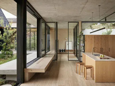 A modern kitchen with wooden cabinets and open shelving, featuring a large window and a concrete floor.