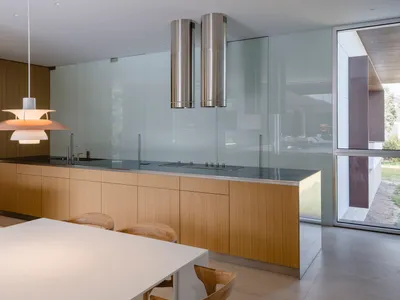 A modern kitchen featuring wood cabinetry, glass backsplash, and stainless steel appliances.