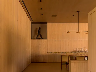A modern, minimalist kitchen with wooden walls and flooring, featuring a dining table and chairs, and a sculpture on the wall