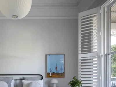 Modern minimalist bedroom featuring a metal-framed bed on a wooden floor with a white plaster ceiling and white window shutte