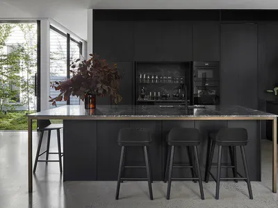 A modern minimalist kitchen featuring a dark wood and marble kitchen island with stools, dark cabinets, and a bar setup.