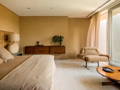 A modern minimalist bedroom featuring neutral textiles, wood accents, and a glass cabinet.