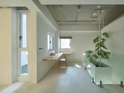 A minimalist home office with concrete and glass elements, featuring a desk, chair, and window.