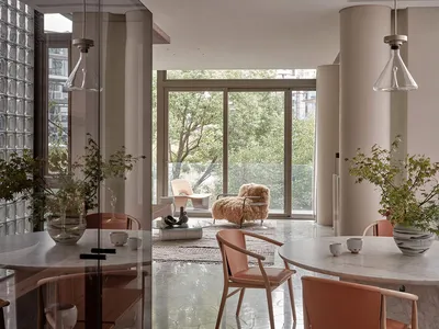 Modern, minimalist kitchen with marble countertops, wooden chairs, and large windows.