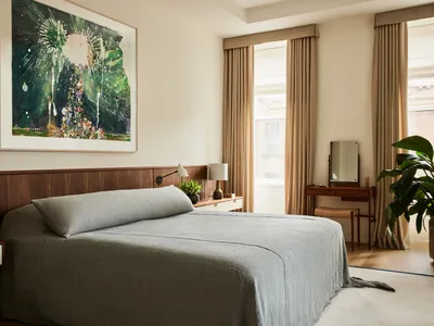 Modern bedroom featuring gray textiles, white accent blinds, and a large painting above the bed.