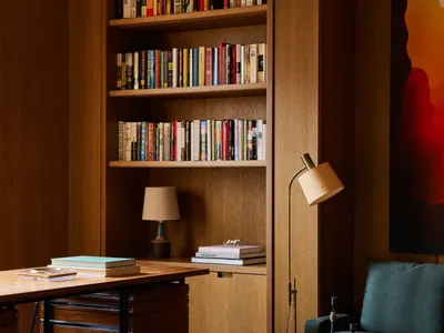 A modern home office with a large wooden bookshelf filled with books, a wooden desk, and a comfortable green armchair.