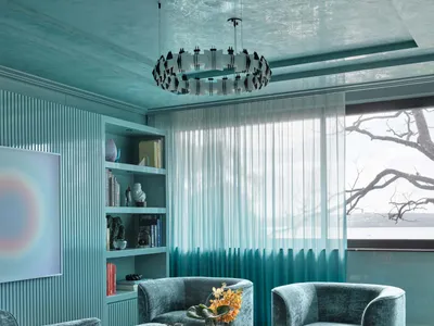 A modern industrial living room with blue upholstered chairs, a black and white geometric rug, and a bookshelf filled with bo