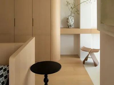 A modern minimalist bedroom with wooden furniture, a black side table, and a vase with green plants on a shelf.