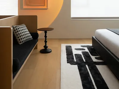 A minimalist bedroom featuring a sleek black platform bed, a black and white geometric rug, a wooden bench with a black and w