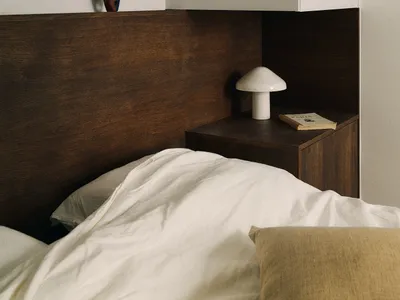 A minimalist bedroom featuring a wooden headboard, ceramic side table, and fabric bedding.