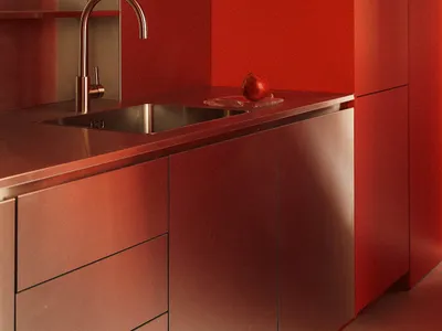 A minimalist kitchen featuring bright red walls, metallic countertops, and stainless steel sink.