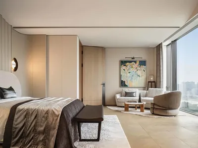 Modern bedroom featuring a bed with fabric bedding and wooden headboard, a small sofa, and a painting on the wall.