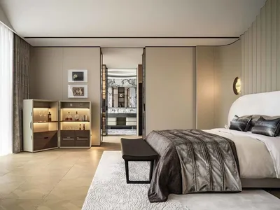 A modern bedroom featuring neutral-colored walls, floors, and furniture, with a large bed and a built-in bar cabinet.