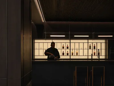 A dark-wood and marble industrial-style restaurant bar with a bartender preparing drinks.