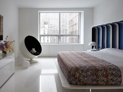A minimalist bedroom featuring a modern bed with a colorful striped headboard and a sleek, white floor and furniture.