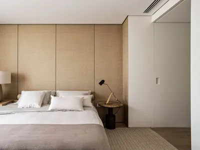 A minimalist bedroom with neutral-toned walls, bed, and bedding, featuring simple and functional design elements.