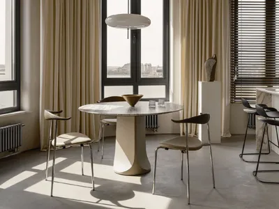 A modern kitchen with marble countertops and floor, featuring wooden chairs and a large round table.