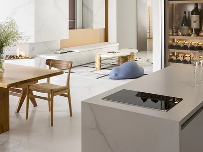 A modern kitchen with white marble countertops, wooden furniture, and a fireplace.