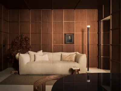 A cozy living room featuring a beige sofa, wooden panel walls, and a framed portrait.