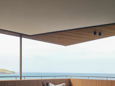 Modern industrial-style living room with a brown leather sofa, wooden coffee table, gray armchair, and large ocean view.