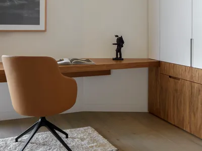 A modern home office space featuring a wooden desk and metal accents, with a comfortable chair and a framed abstract painting