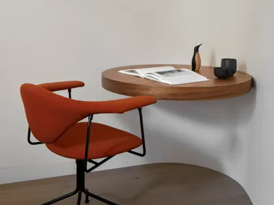 Modern home office setup with a round wooden table, orange chair, and pendant light.