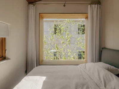 Minimalist bedroom with white bed, large window, and green leaves outside