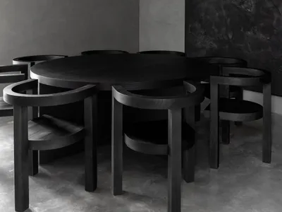 A minimalist black and wood restaurant dining room with a round table and chairs.