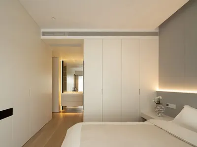 Modern minimalist bedroom with white furniture and wooden floor.