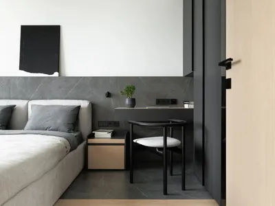 A minimalist bedroom featuring a bed with white bedding and a black headboard, accompanied by a small desk with a black chair