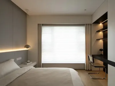 A minimalist bedroom featuring a taupe bed, a built-in desk, and neutral-toned curtains.