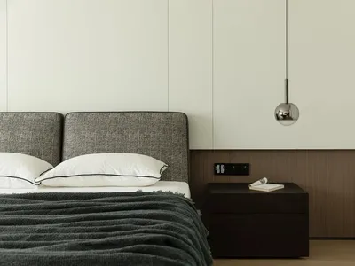 A minimalist bedroom with a fabric bed and metal pendant light.