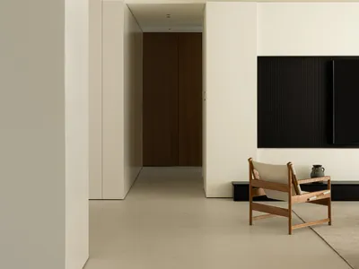 A minimalist living room featuring concrete walls and flooring, with a wooden chair and black television setup.