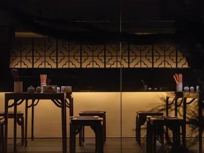 A modern restaurant interior featuring wooden tables and stools with a warm, ambient lighting setup.