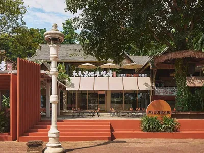 A restaurant exterior made of brick and wood with white parasols and green trees in the background.
